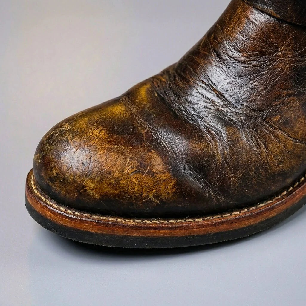 Rounded toe and welted sole of brown distressed leather engineer boots, close up